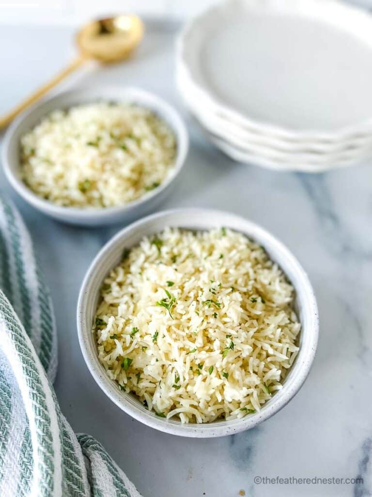 Two white bowls of Instant Pot Rice with a stack of white plates, striped cloth, and golden serving spoon at the background.