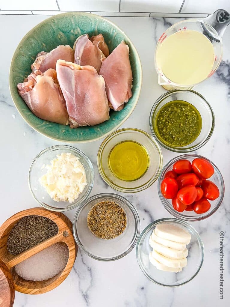 ingredients for making Instant Pot Pesto Chicken which includes boneless chicken thighs, chicken broth, pesto sauce, olive oil, cream cheese, salt and pepper, cherry tomatoes, mozzarella cheese, and all purpose seasonings.
