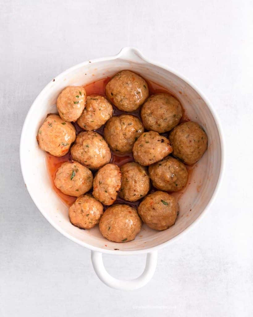 a white mixing bowl with meatballs and sweet chili sauce