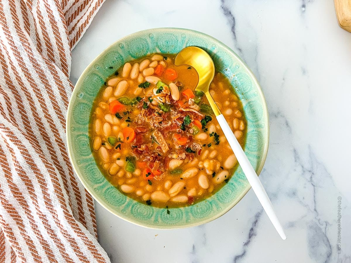 White legumes with ham, stock, and seasonings in a green bowl.