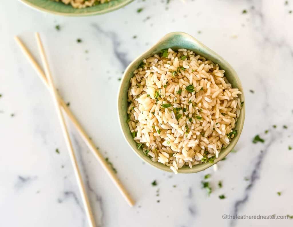 Chopsticks placed next to bowl of fluffy grains garnished with chopped cilantro.
