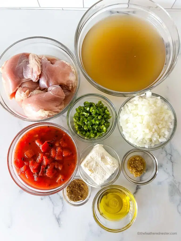 ingredients for making creamy chicken tortilla soup which consists of chicken stock, chicken breast tenders, jalapeno peppers, onion, garlic, fire roasted diced tomatoes, cream cheese, cumin, and olive oil.