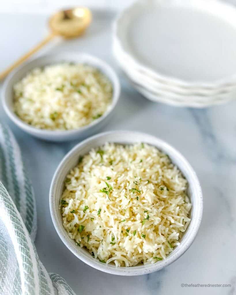 Instant Pot coconut rice in a bowl on a striped kitchen towel next to another Instant Pot side dish. Large serving spoon and stack of plates in background.