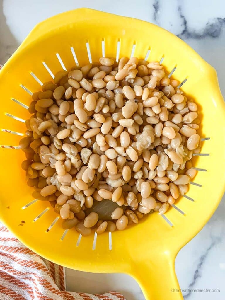 dry great northern beans in a yellow colander.