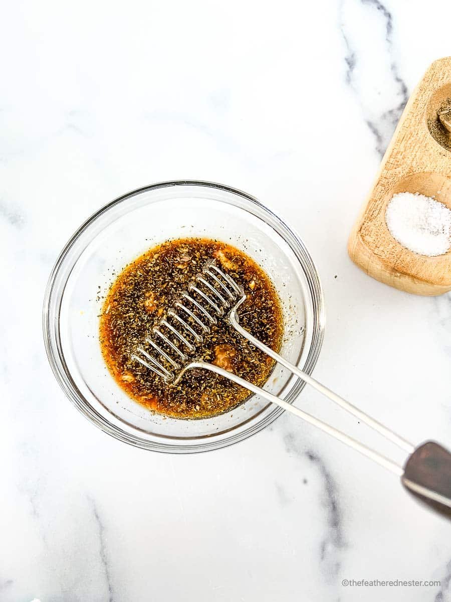 Whisking the balsamic vinegar marinade for chicken ingredients in a clear bowl with a salt and pepper cellar in the background.