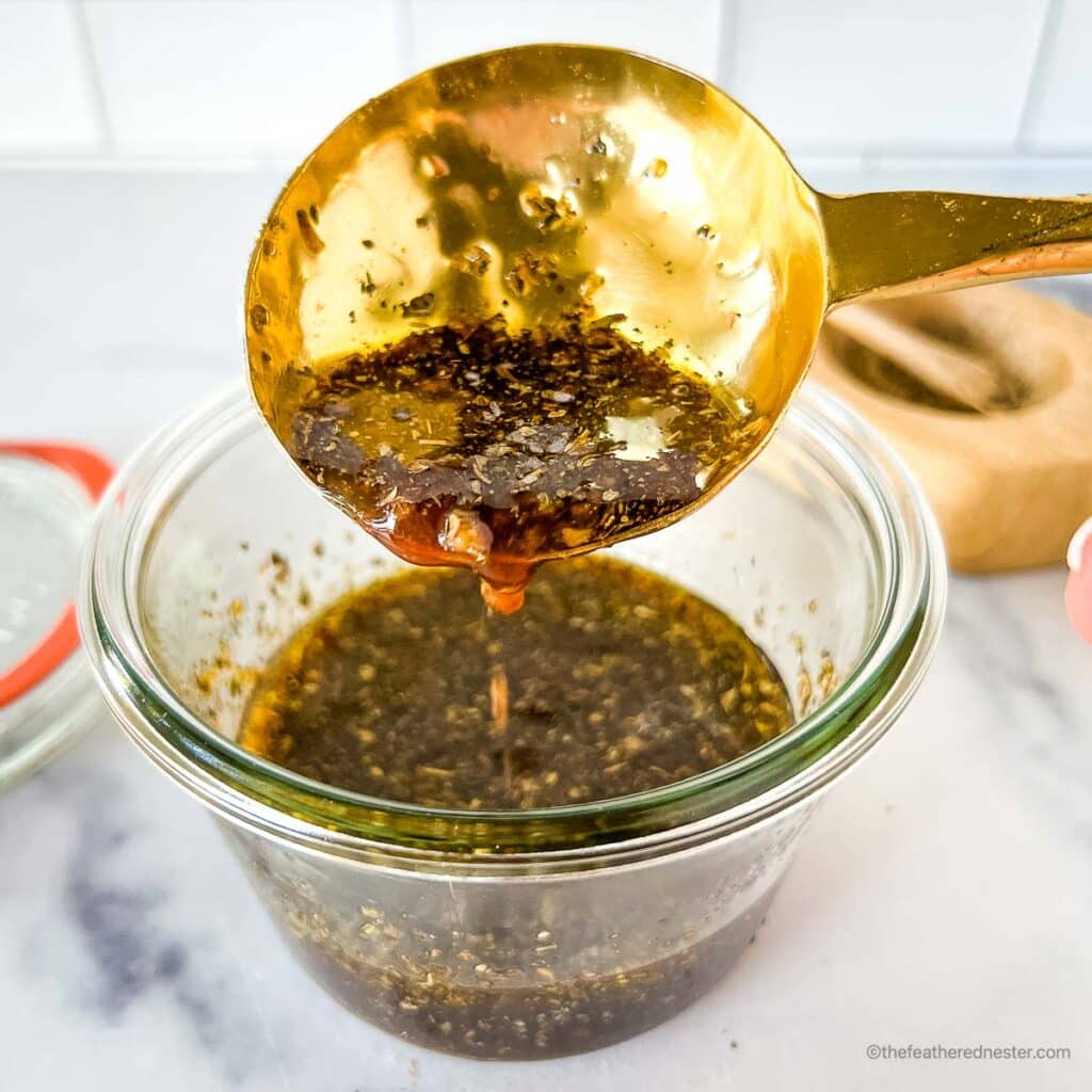 a close up photo of a golden spoon scooping the Balsamic chicken marinade in a glass jar with its lid and a salt cellar in the background.