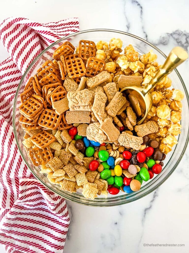 a clear bowl with Chex party mix with M&Ms and golden scoop