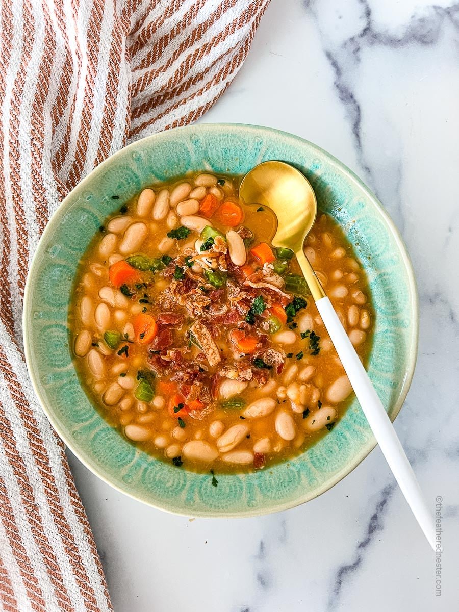 A green bowl of great northern bean soup with a spoon in it.