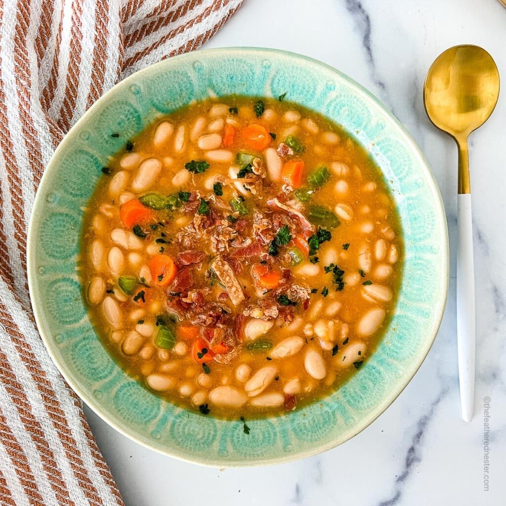 a green bowl with great northern bean soup with a golden spoon and a striped red kitchen towel at the side.