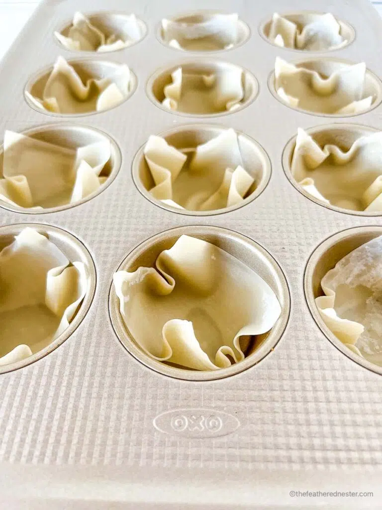 wonton wrappers all lined up in a muffin pan.