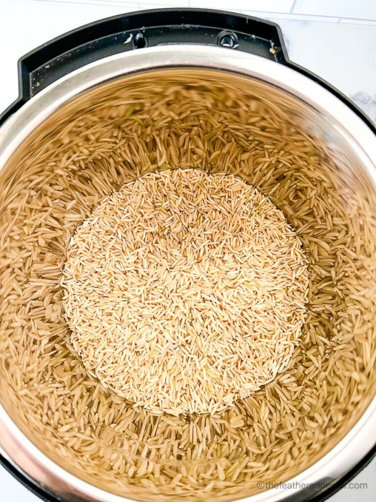 Uncooked brown basmati rice poured into a pressure cooker.