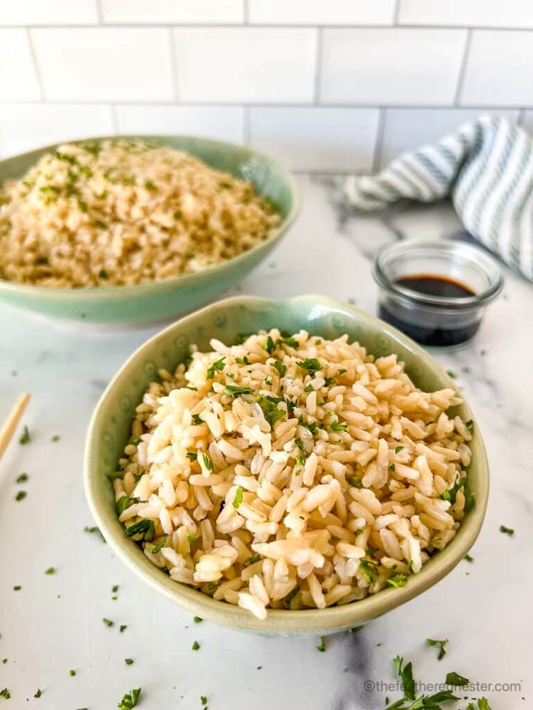 a small and large green bowls with Instant Pot brown rice garnished with chopped cilantro with a soy sauce in a small bowl, striped cloth in the background.