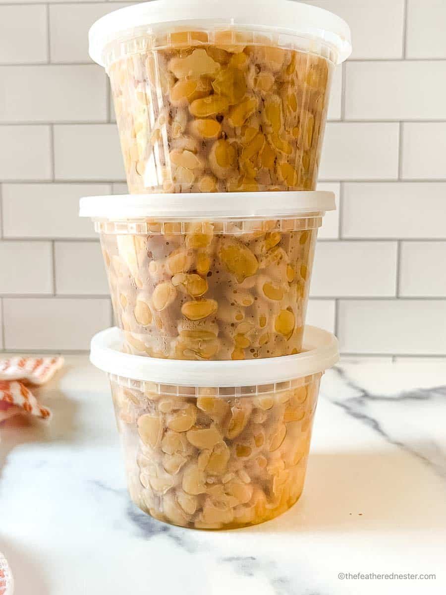 A stack of 3 plastic containers with cooked Great Northern beans inside.