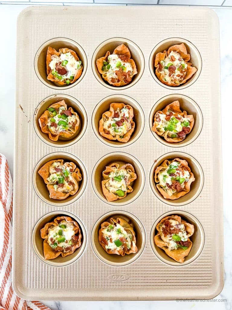 Jalapeno popper filling mixture inside the wonton cups on a muffin pan.