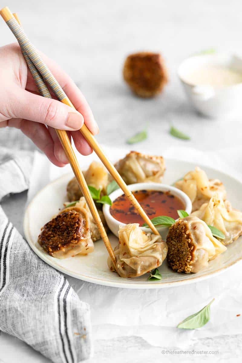 Hand holding filled wonton appetizer in chopsticks