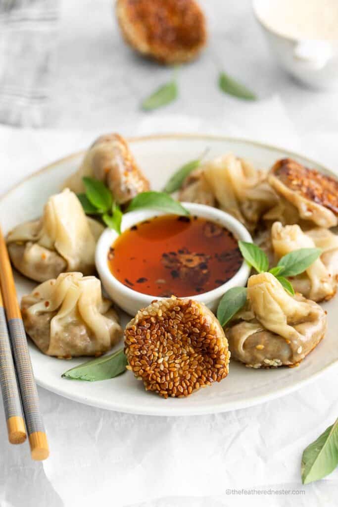 mushroom vegetarian dumplings and garlic chili oil on a white plate with chopsticks on the side.