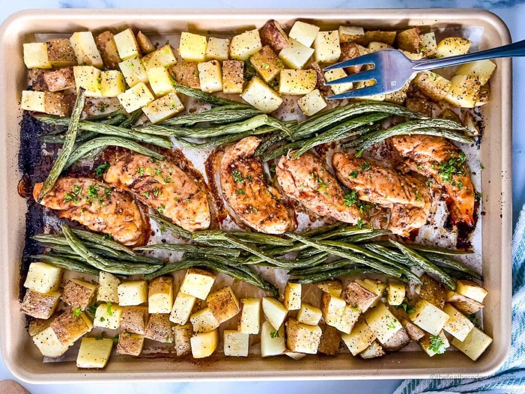 a baking sheet with baked chicken tenders, asparagus, and potatoes.