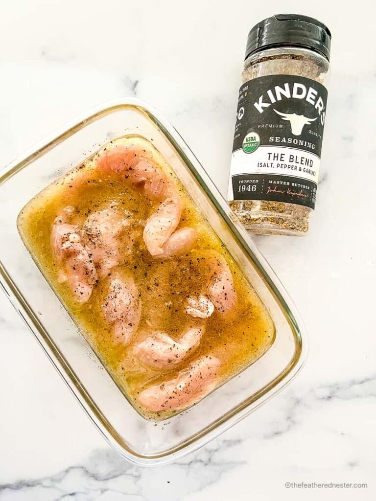 a glass container with marinated chicken tenders and a bottle of Italian seasoning beside it.