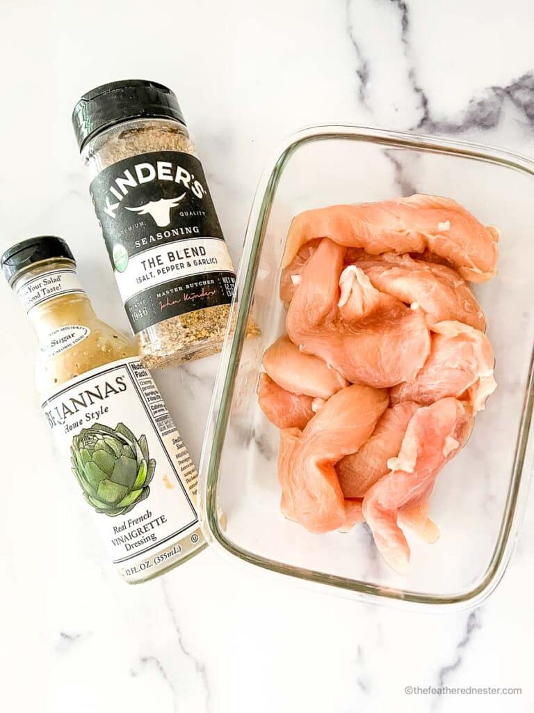 Ingredients for making Oven Baked Marinated Chicken Tenders which contains chicken tenders, Italian seasoning, and a vinaigrette dressing.