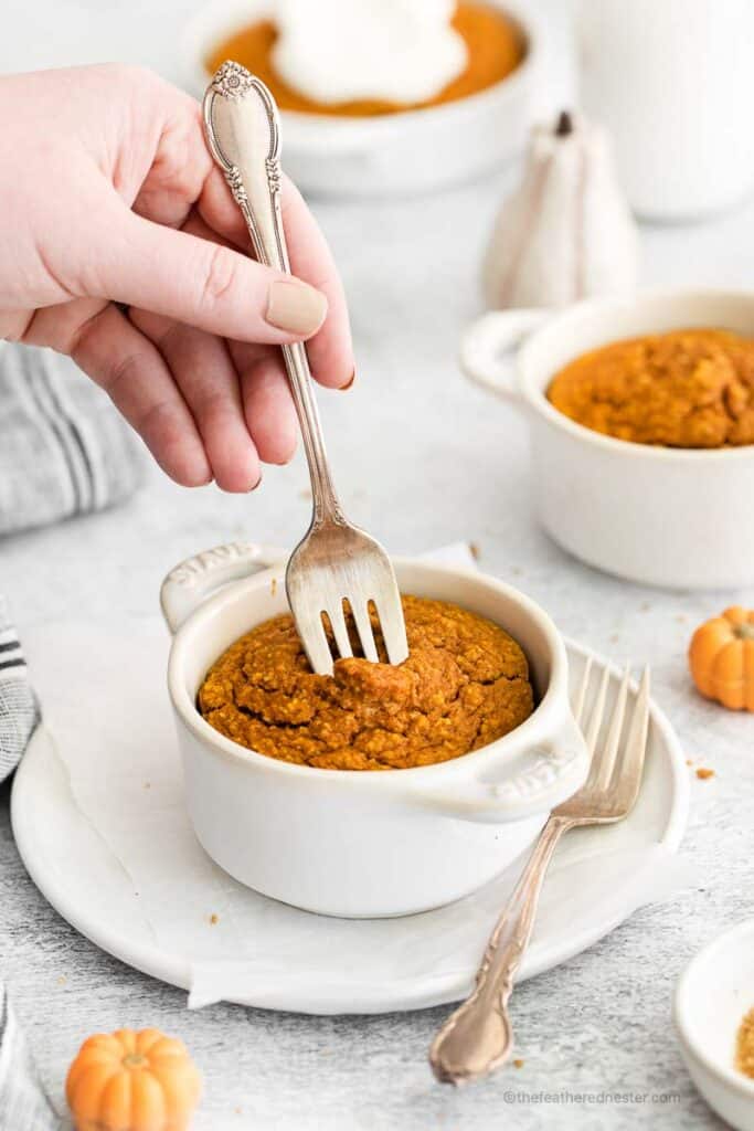 a hand holding a fork poking the pumpkin spiced oatmeal inside a ramekin with another ramekins in the background.