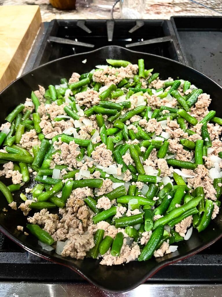green beans, onions, garlic, and ground beef all mixed in together in a cast iron skillet. 