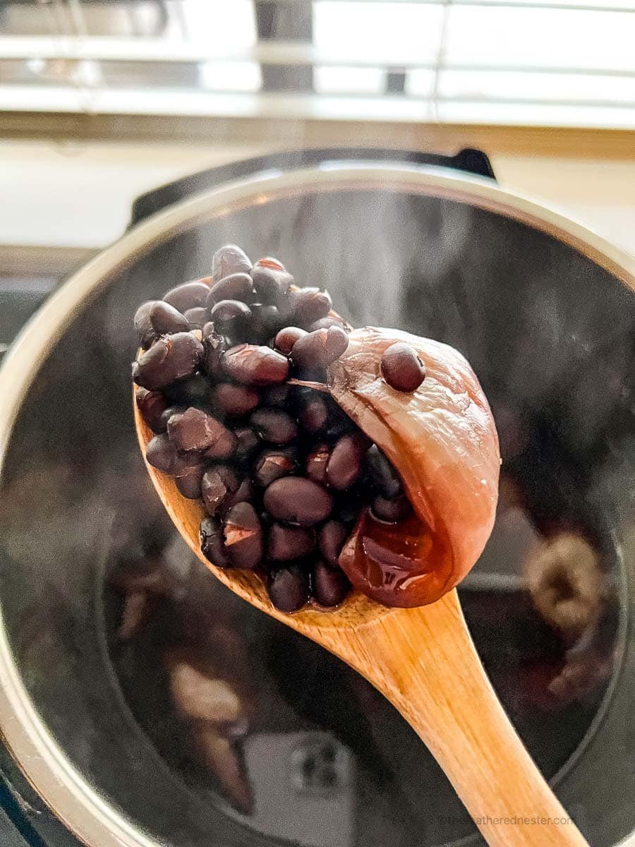 A scoop of cooked black beans using a wooden spoon in an Instant Pot.