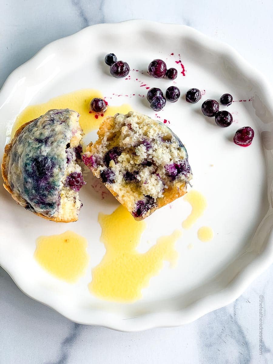 a white plate with blueberry muffin and pieces of blueberries.