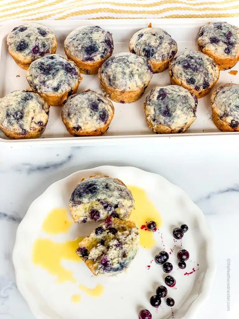 a white serving tray with blueberry muffins and a white plate with a Bisquick blueberry muffins and blueberry fruits on it.