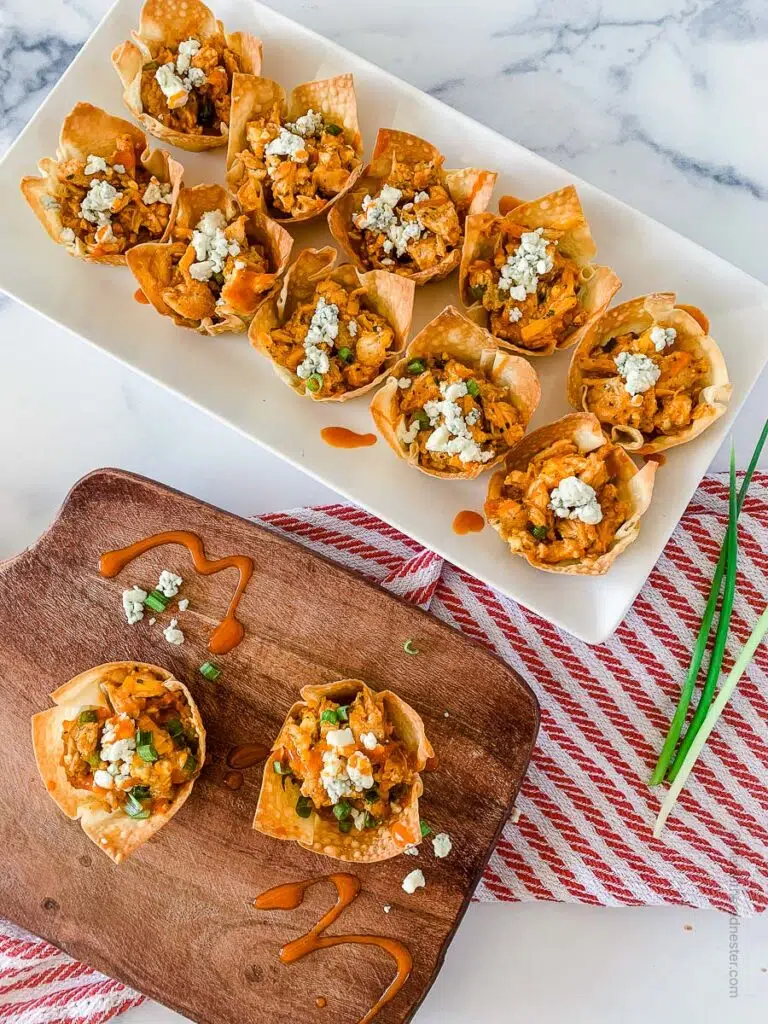 top view photo of buffalo chicken wonton cups placed in a wooden serving tray and white serving plate.