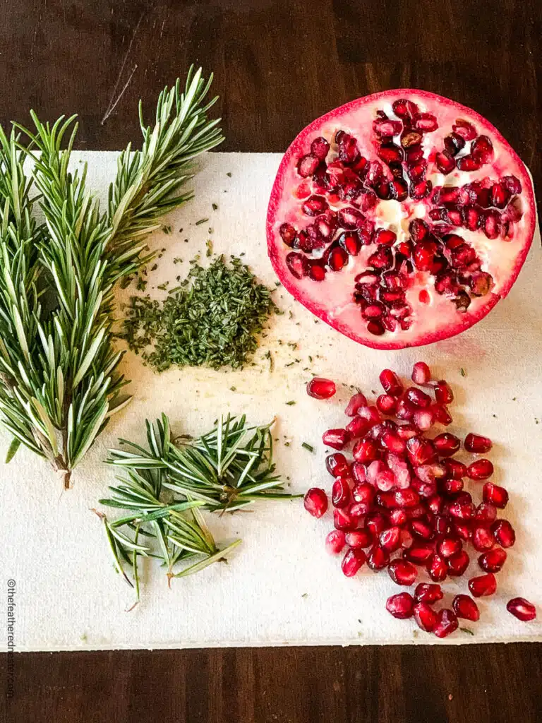 1/2 of a pomegranate, a pile of seeds, and springs of rosemary