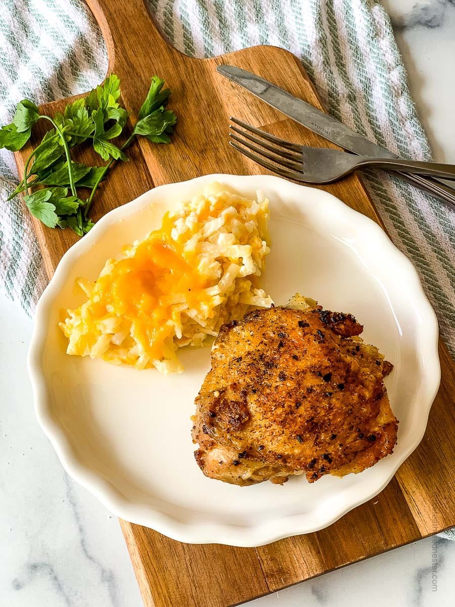 a white plate with cast iron skillet chicken thighs and hash brown placed on top of a wooden board.