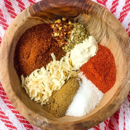 homemade taco seasoning ingredients all placed in a wooden bowl and a striped red kitchel towel beneath it.