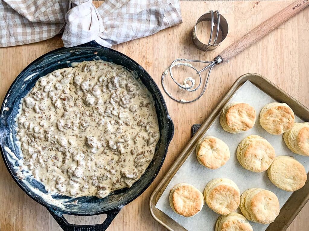 a cast iron skillet of gravy sausage with a pan of freshly baked biscuits