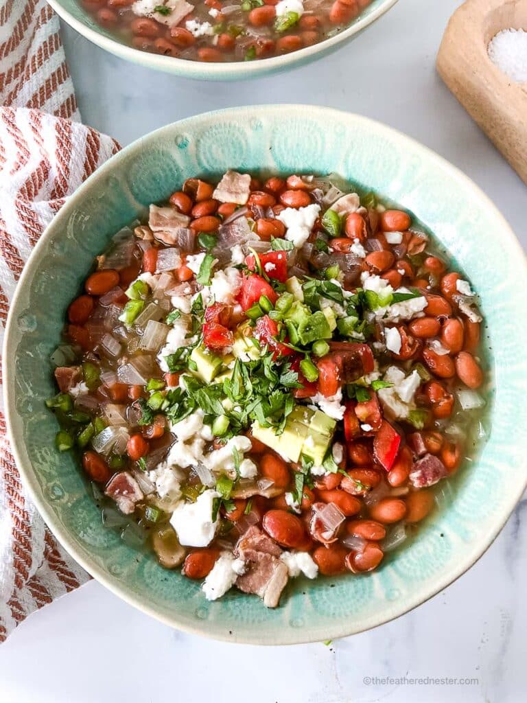 a close up photo of two green bowls of crock pot pinto beans with ham with a striped red cloth and a salt and pepper cellar at the side.