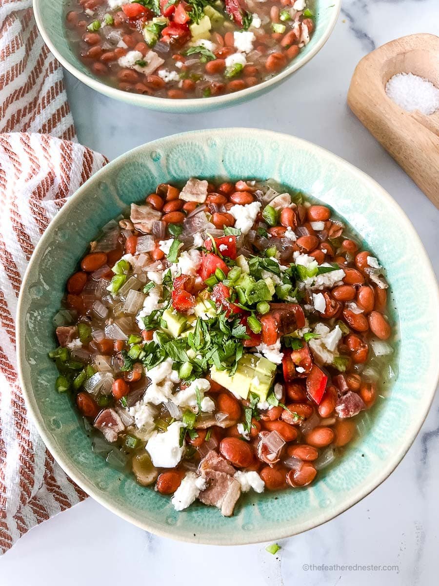 a close up photo of two green bowls of crock pot pinto beans with ham with a striped red cloth and a salt and pepper cellar at the side.