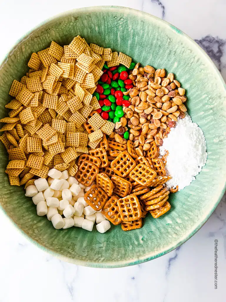 a green bowl with all the ingredients needed to make the Christmas Chex Mix recipe.