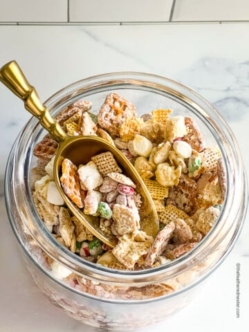 A jar of Christmas Chex Mix with golden scoop.