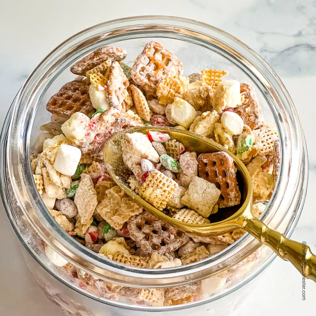a jar with Christmas Chex Mix with a golden scoop.