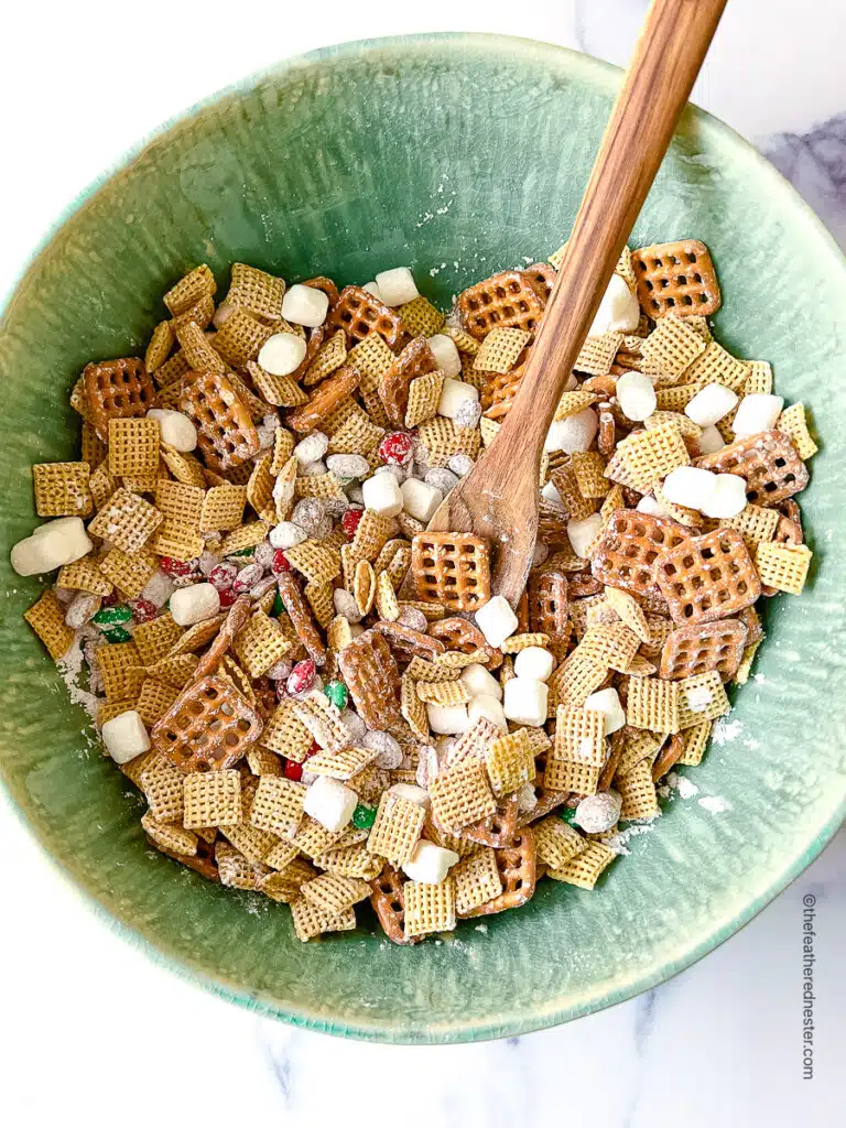 a green bowl with Christmas Chex Mix with a wooden spoon.