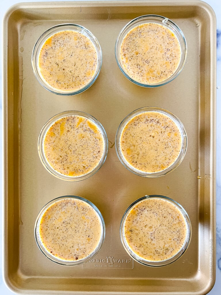 Unbaked custard in small glass bowls, sitting on a baking sheet.