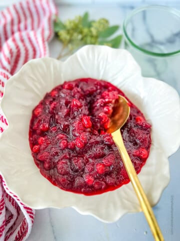 a white bowl of cooled and thickened cranberry sauce ready to serve with a gold serving spoon