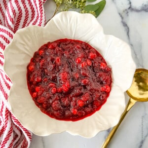 a white bowl of cooled and thickened cranberry sauce ready to serve with a gold serving spoon