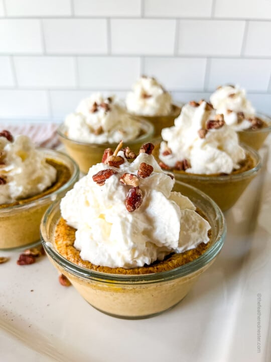 six cups of pumpkin custard and with whipped cream and nuts on top.