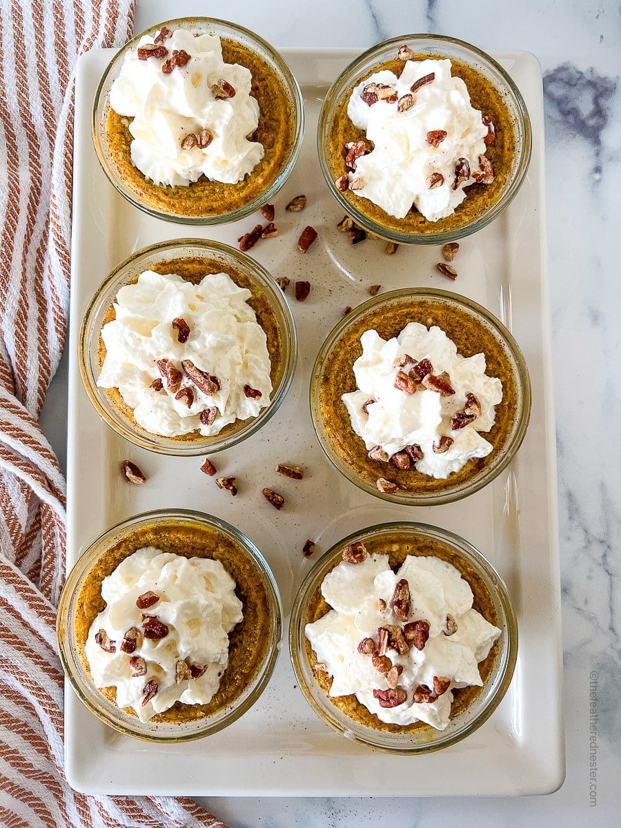 white serving platter with 6 individual servings of pumpkin custard with nuts and whipped cream on top.