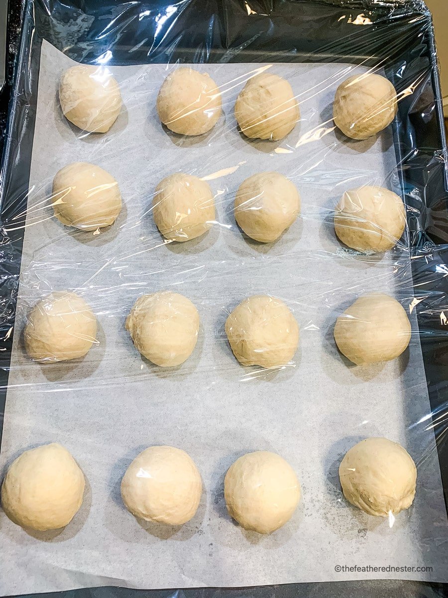 Dough balls on a parchment paper lined baking sheet covered with a plastic wrap.