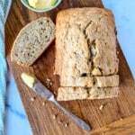 square photo of Bisquick Banana Bread with a bowl of butter and bread knife on top of a wooden board.