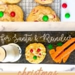 A vertical image with the title "christmas M&M COOKIES" at the bottom. The image is split, showing baked M&M cookies with red and green candies on a cooling rack on the top, and a wooden sign that reads "for Santa & Reindeer" below, next to a cookie, milk, and carrot cutouts. The website "TheFeatheredNester.com" is at the bottom.