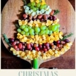 A vertical image with the title "CHRISTMAS tree appetizer" at the bottom. The main image shows an appetizer board creatively arranged on a wooden serving board to look like a Christmas tree using cubes of yellow and white cheese, red and green grapes, and fresh rosemary sprigs for boughs. The website "TheFeatheredNester.com" is at the bottom.