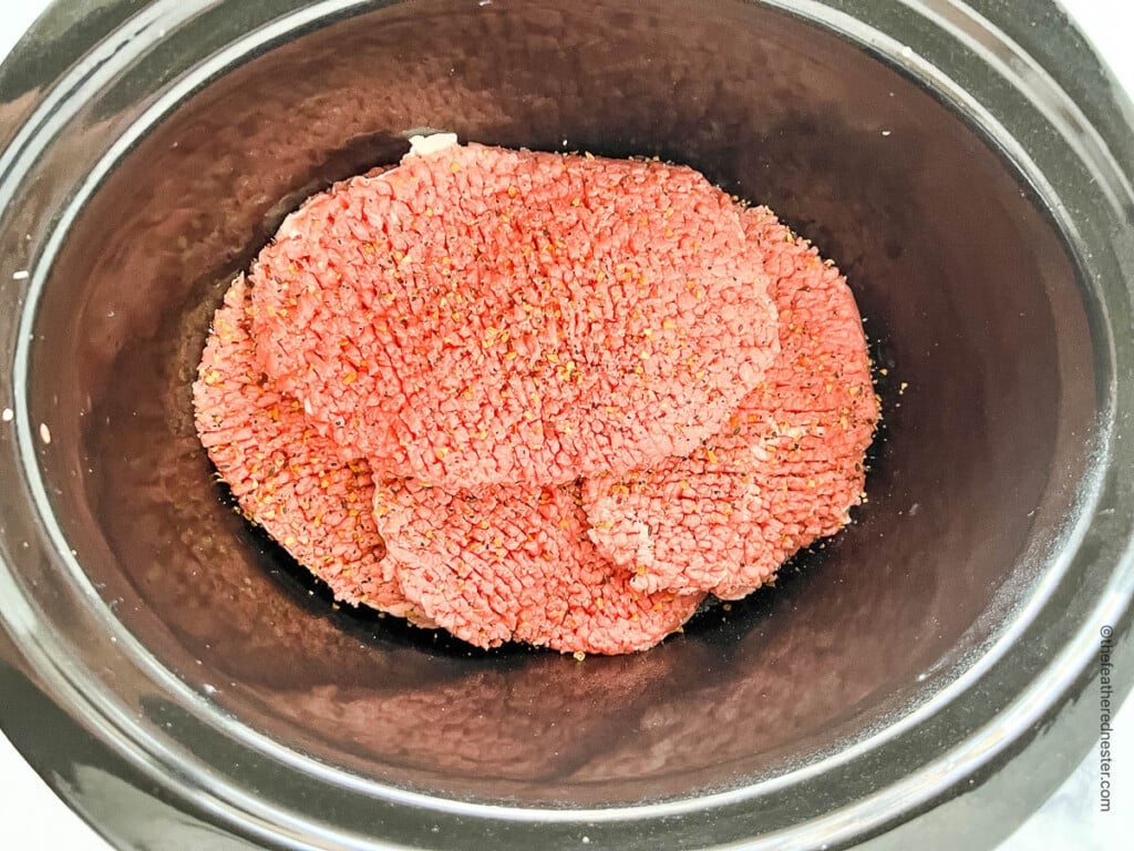Raw cube steak in a slow cooker.