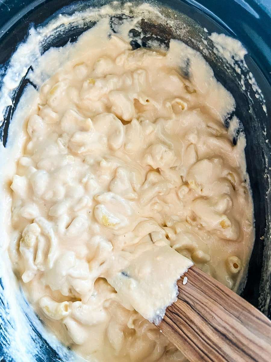 using a wooden spoon to stir 3 cheese mac and cheese in a crock pot.